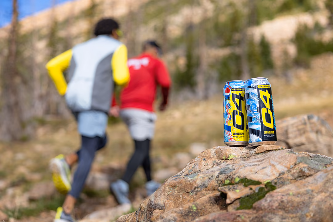 Two trail runners on a mountain with C4 energy drinks in focus in the foreground