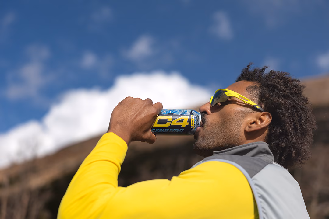 Man drinking C4 energy drink on a mountain wearing yellow trail gear