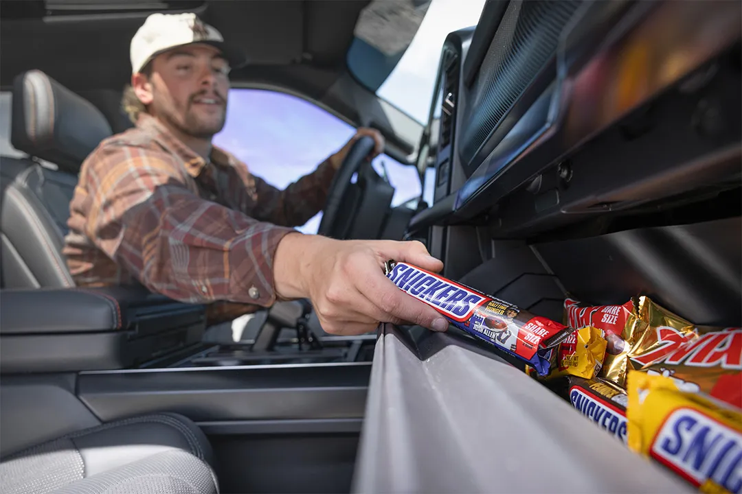 Man reaching for a SNICKERS® candy bar in Raptor Rampage prize vehicle glove box